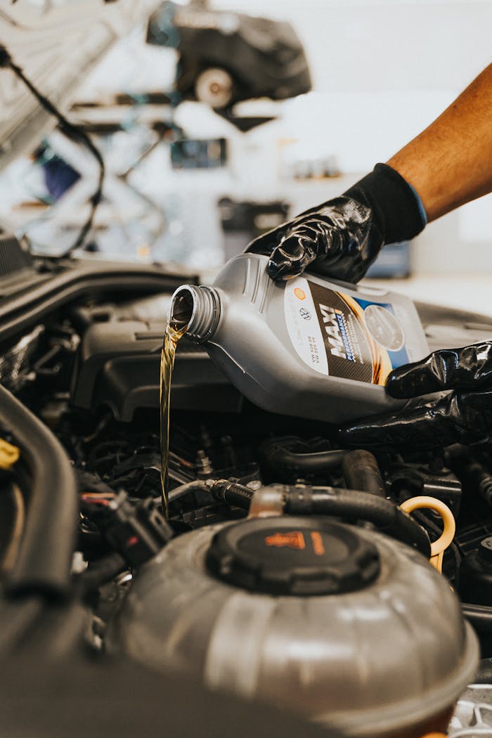 Services A close-up of a mechanic in gloves pouring engine oil into a car engine, showcasing automotive maintenance.