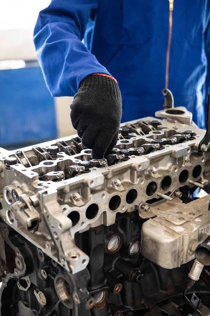 Services Close-up of a mechanic in gloves working on a car engine cylinder head in a workshop setting.